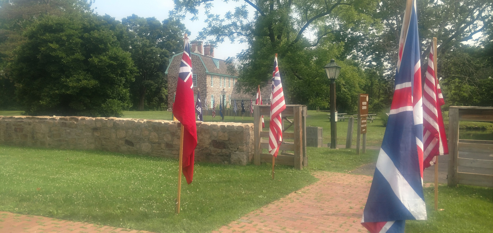 colonial flags in foreground with stone wall behind and stone house further back in center