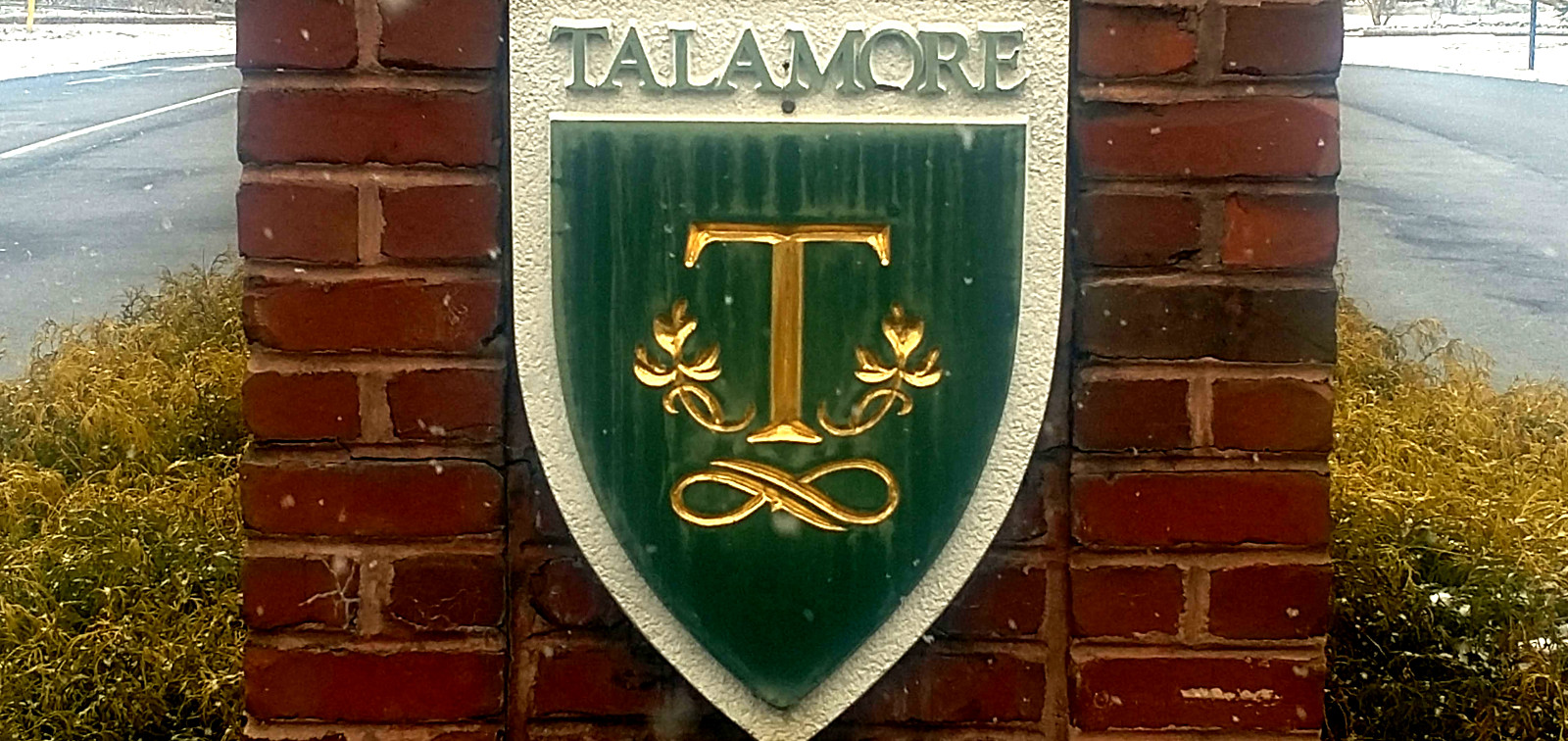 sign on brick pedestal with word Talamore above and large gold letter T in middle of green shield below
