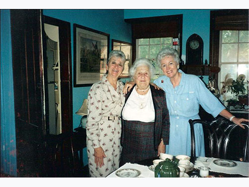 photo of 3 women with arms around each other behind dining table