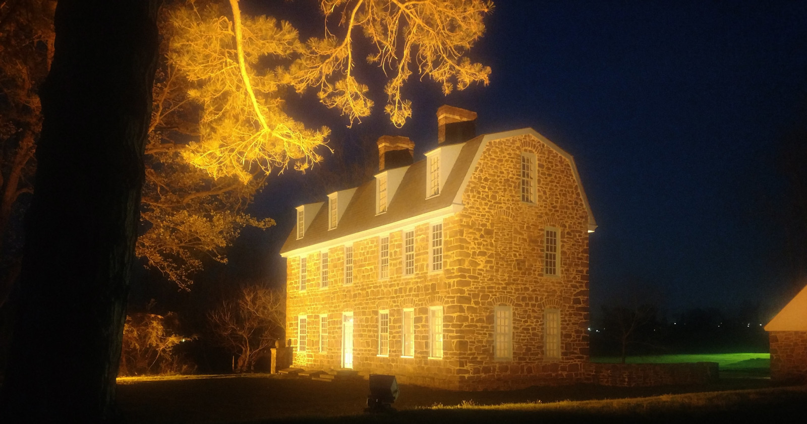 stone building front lit with dark sky, tree to left 