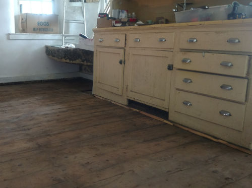 Original pine floor in the 1856 kitchen and 1920s era yello cabinets to right and stone sink in center