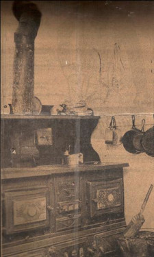 photo of coal stove wit frying pans on wall beside it and coal bucket and shovel in front