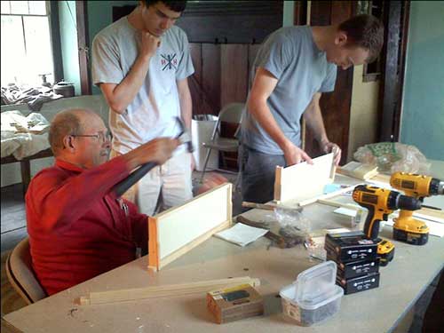 photo of Pete, Tim, Connor building bee hives at the table in the 1721 room at the Penrose Strawbridge House